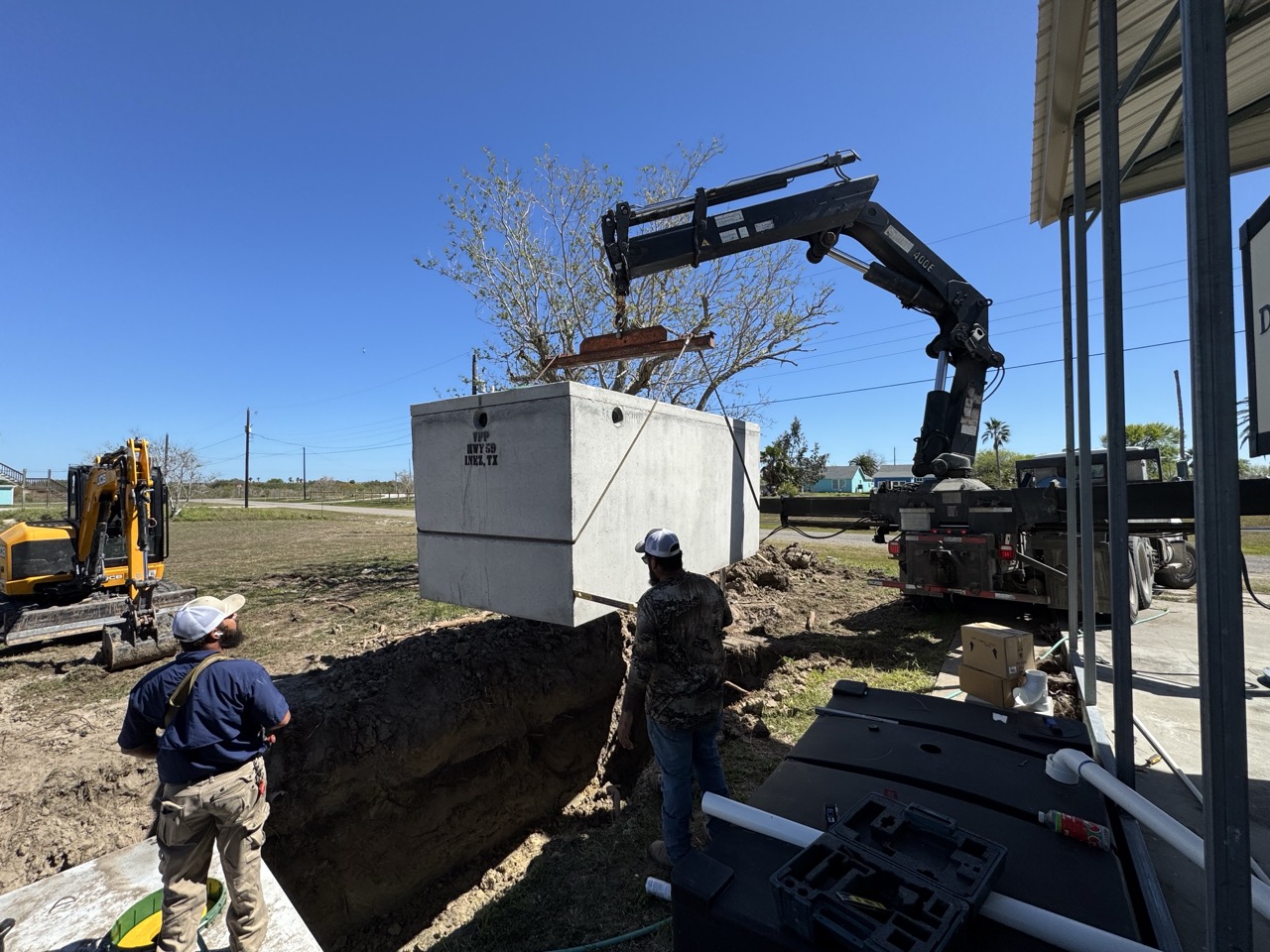 Crew setting a concrete septic tank with a knuckle-boom crane